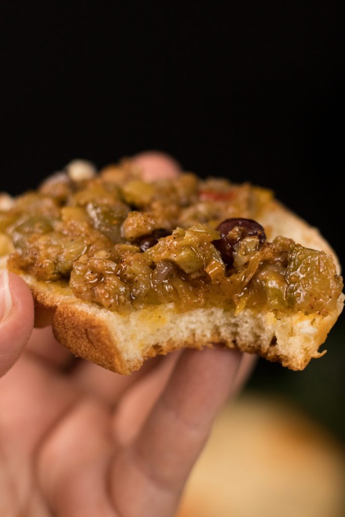 foto de uma mão segurando uma fatia de pão de batata doce servida com caponata